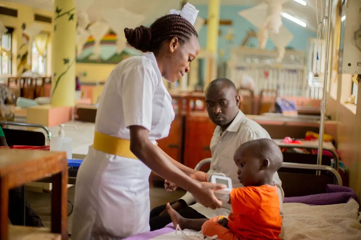 A nurse checking a child's blood pressure on a hospital ward while a parent looks on.