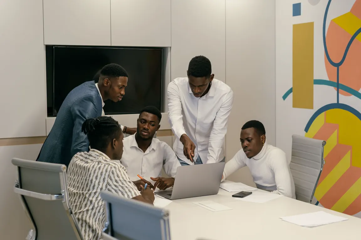A team of colleagues gathered around a laptop in a meeting room.